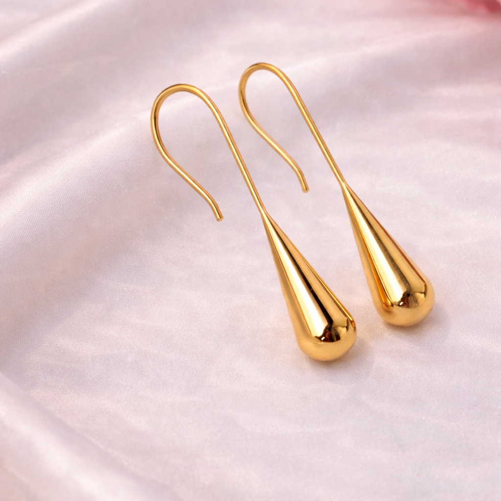 Gold teardrop earrings on a satin surface with pink flowers in the background