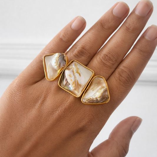 Hand wearing three gold rings with stone inlays on a white background