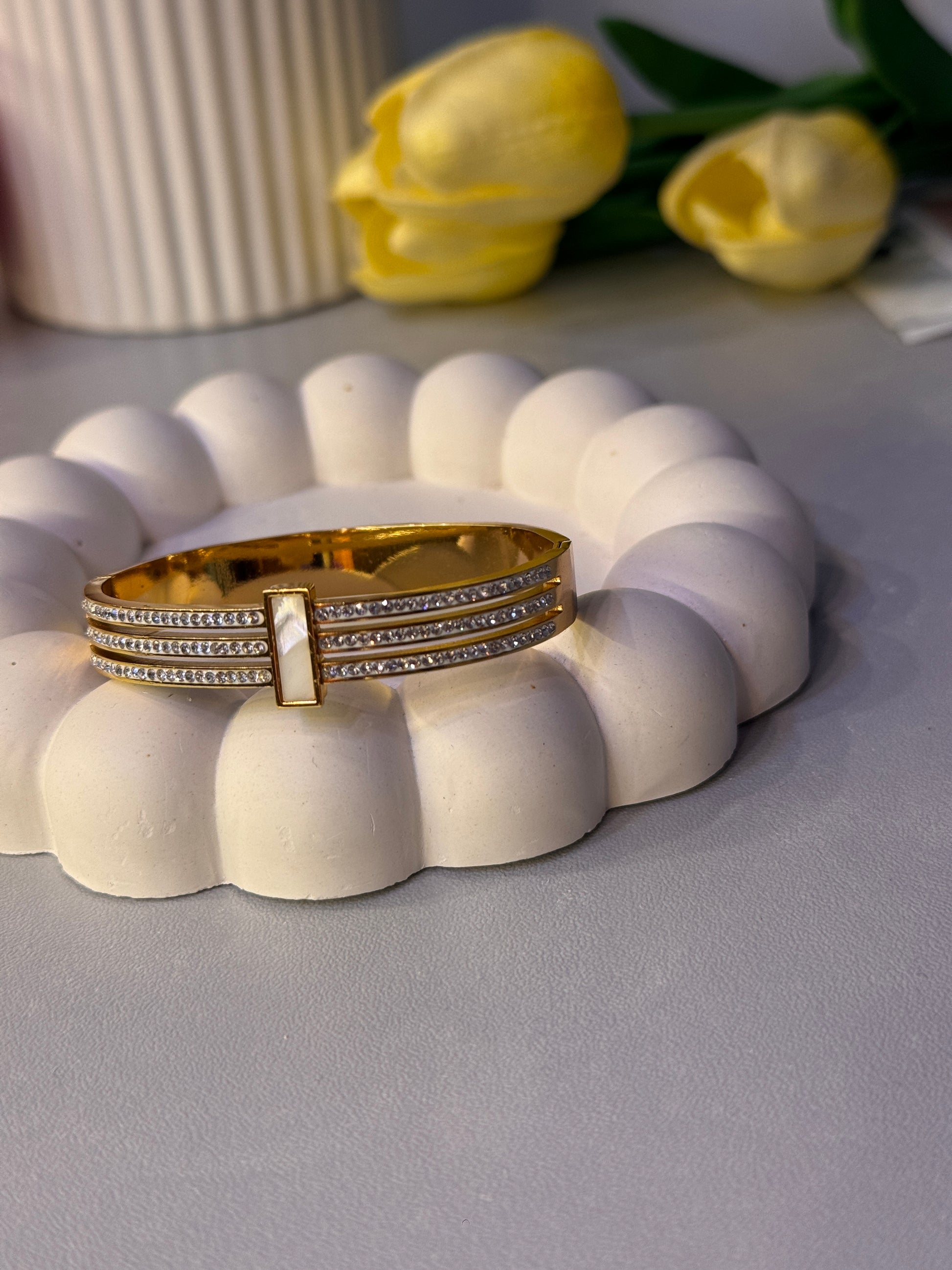 Gold ring with diamonds on a white textured surface with yellow tulips in the background