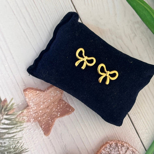 Gold bow-shaped earrings on a black pillow with decorative elements on a light wooden surface.