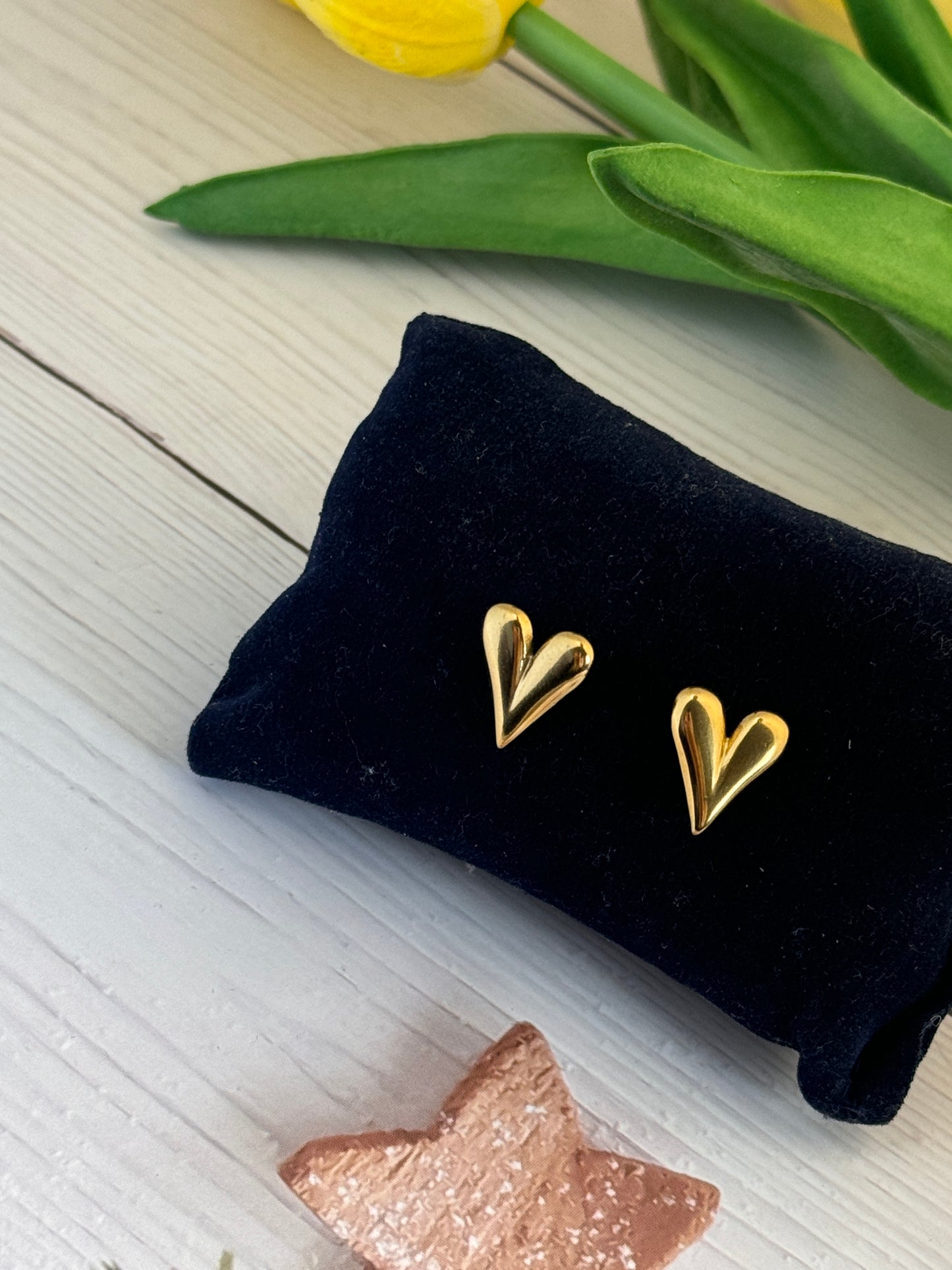 Gold heart-shaped earrings on a black pillow with tulips and a starfish in the background.