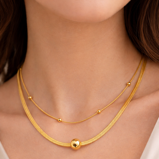 Close-up of a person wearing two gold necklaces on a plain background