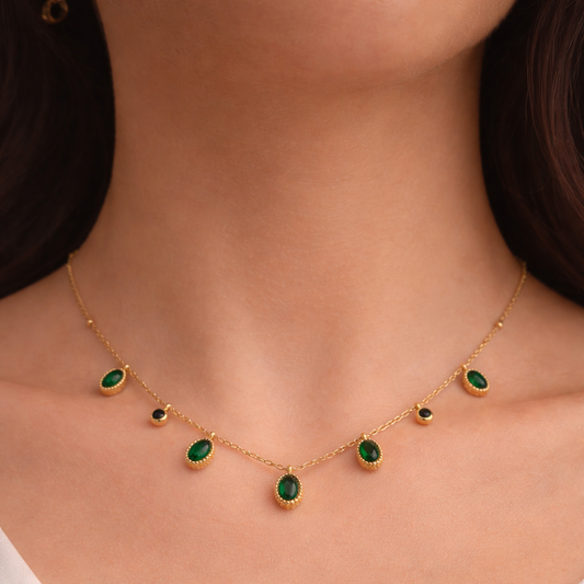 Gold necklace with green gemstones worn by a person in a white top