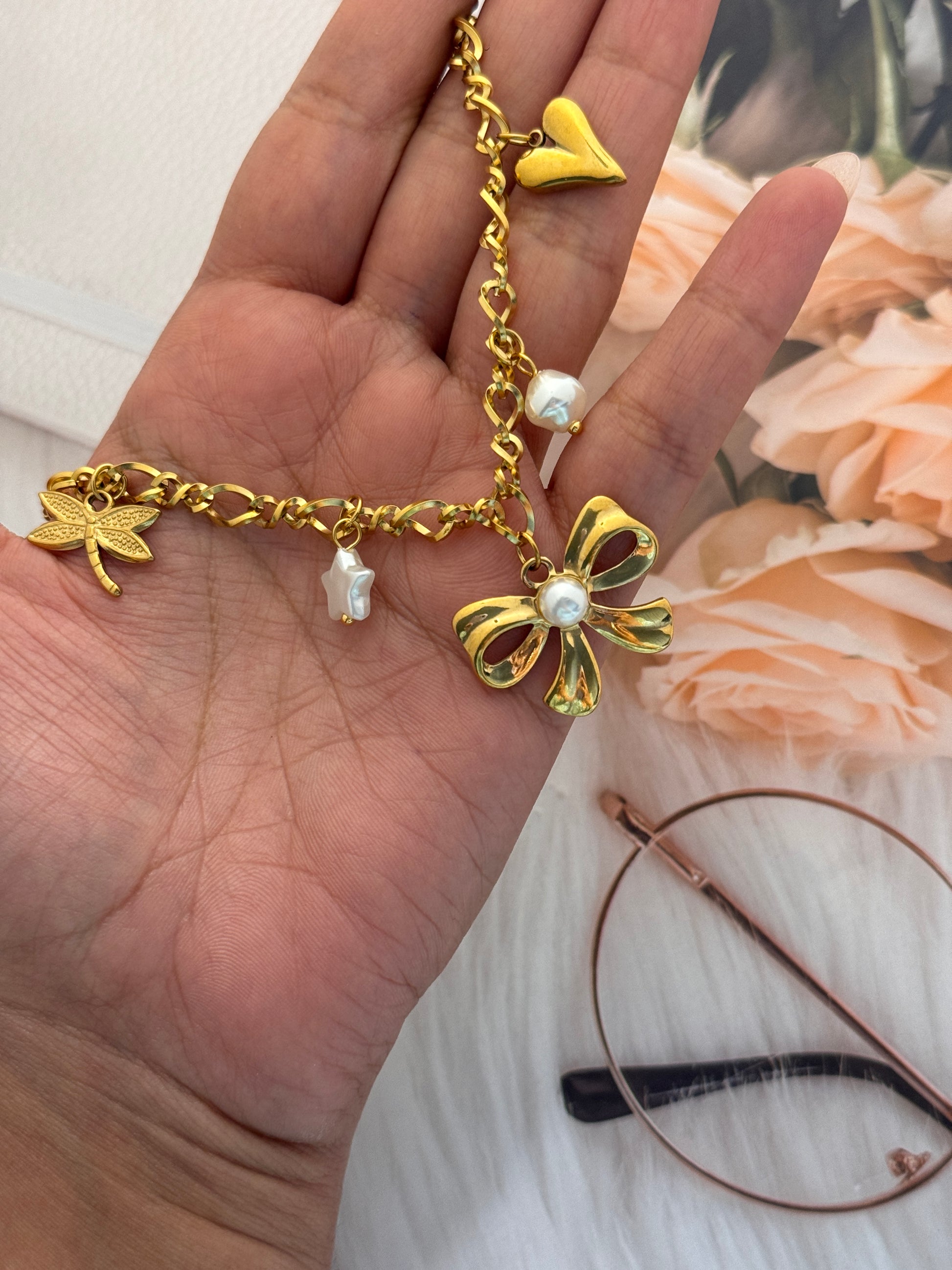 Gold chain bracelet with floral designs held by a hand, with flowers in the background.