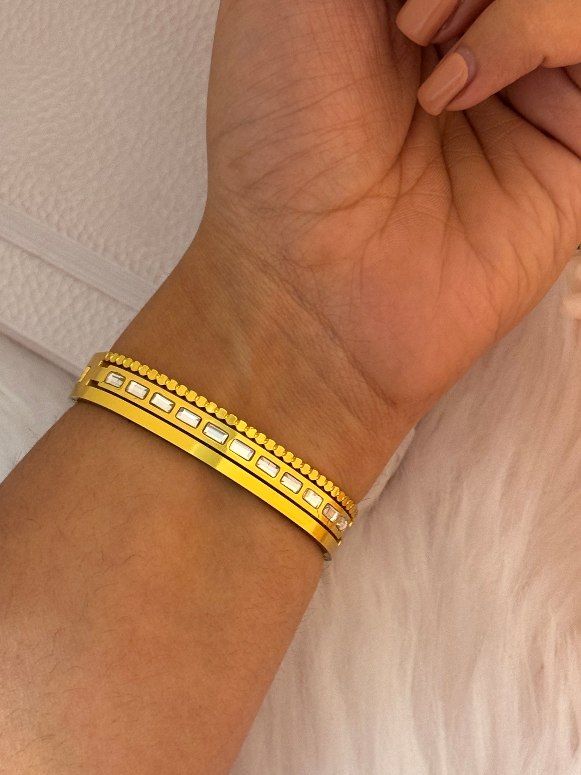 Gold bracelet with embedded stones on a wrist against a neutral background