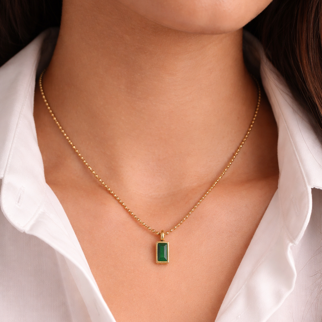 Gold necklace with a green gemstone worn by a person in a white shirt.