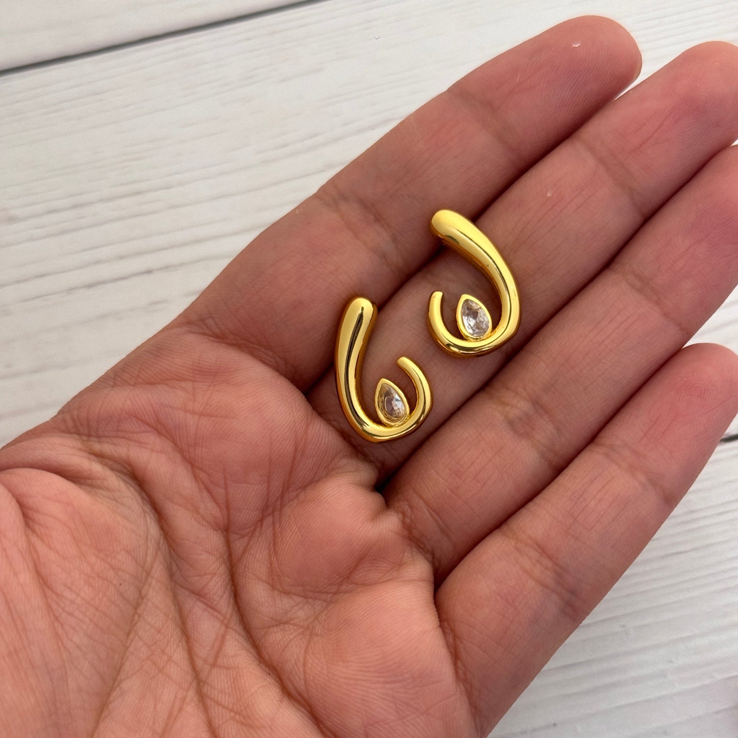 Gold earrings with gemstones held in a hand on a white background