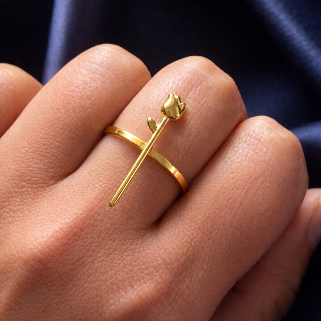 Gold ring with a unique design on a hand against a dark blue fabric background