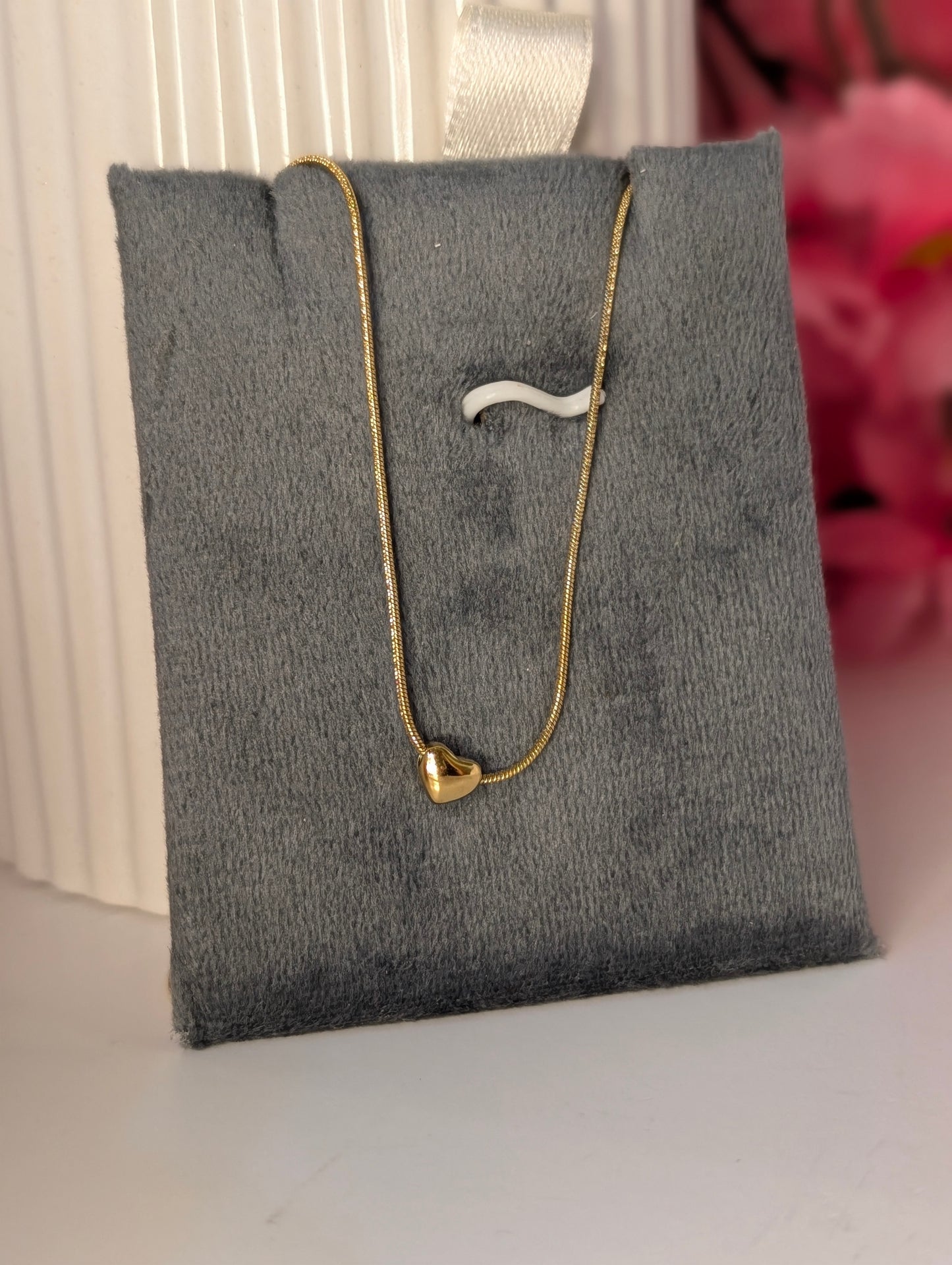 Gold necklace with a heart pendant on a gray jewelry display pillow.