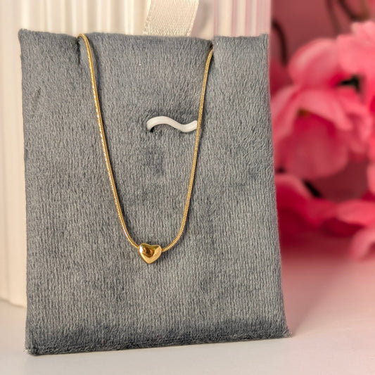 Gold necklace with a heart pendant on a gray jewelry display pillow against a pink floral background