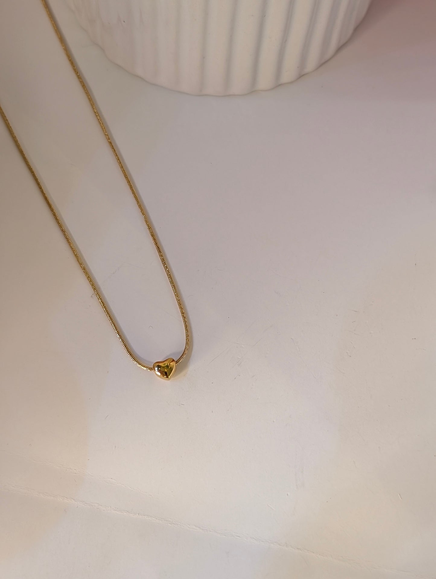 Gold necklace with a heart-shaped pendant on a white surface