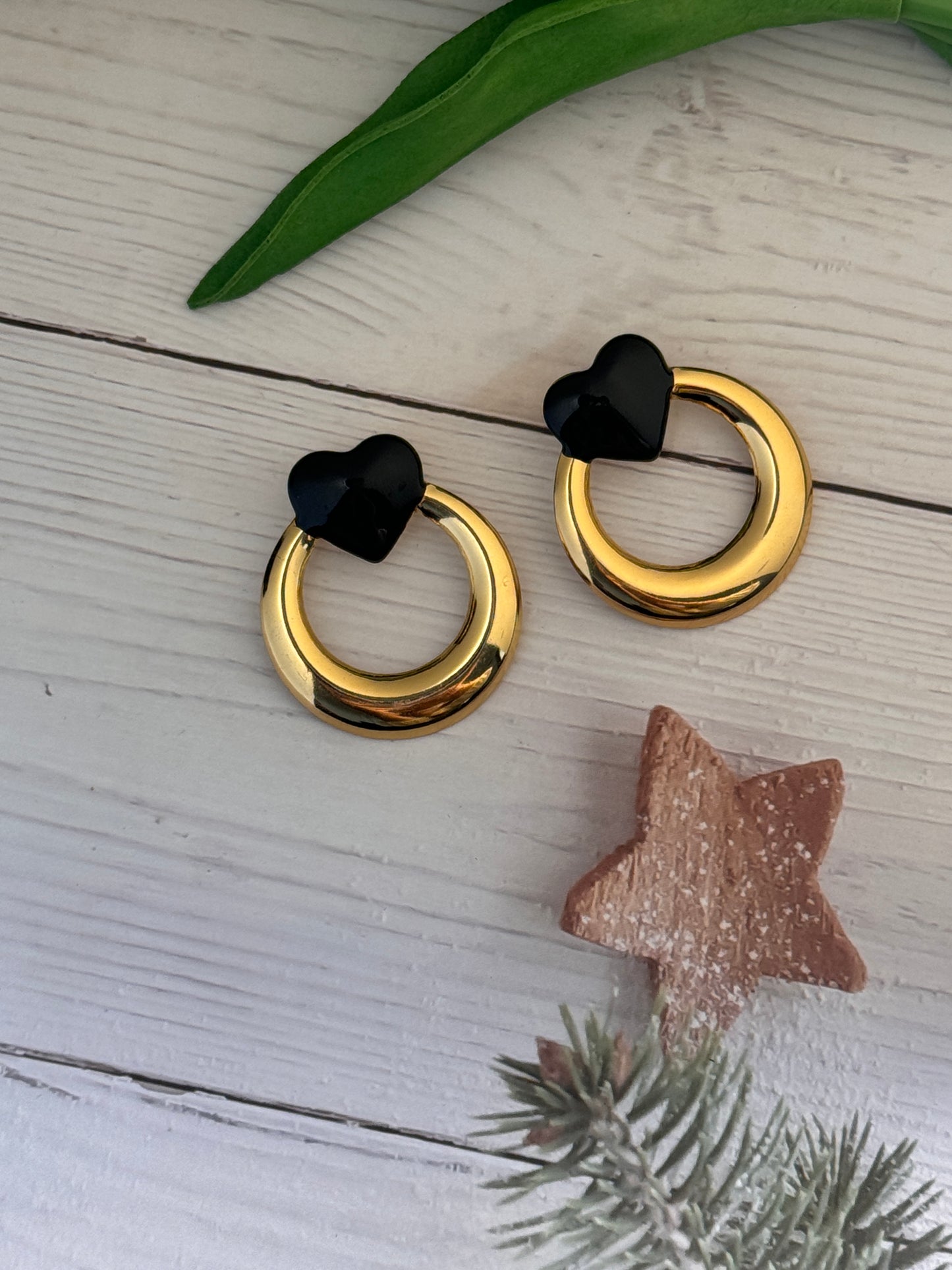 Gold earrings with black heart-shaped centers on a light wooden surface with decorative elements.