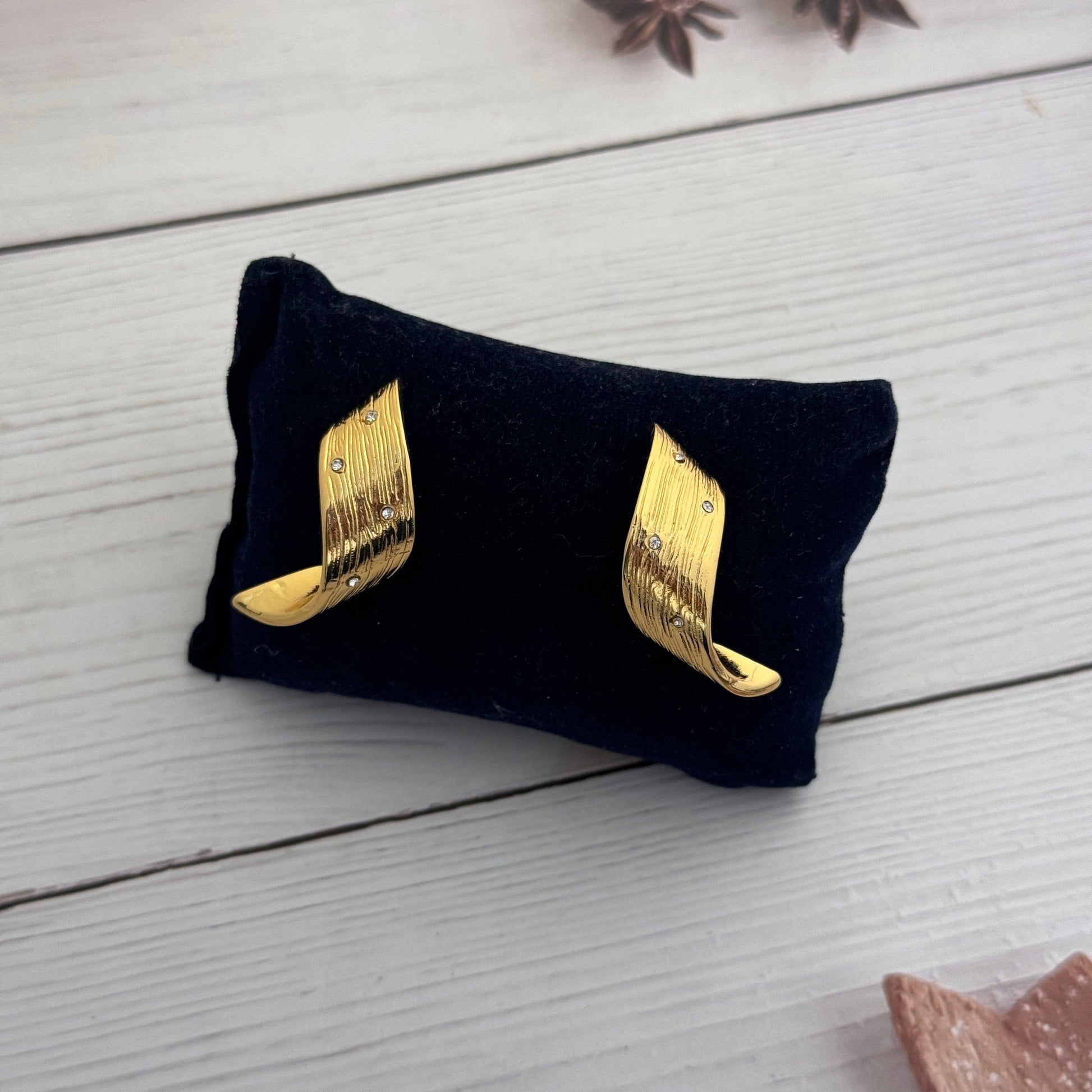 Gold wing-shaped earrings on a black cloth with a white wooden background