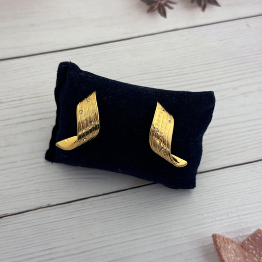 Gold wing-shaped earrings on a black cloth with a white wooden background