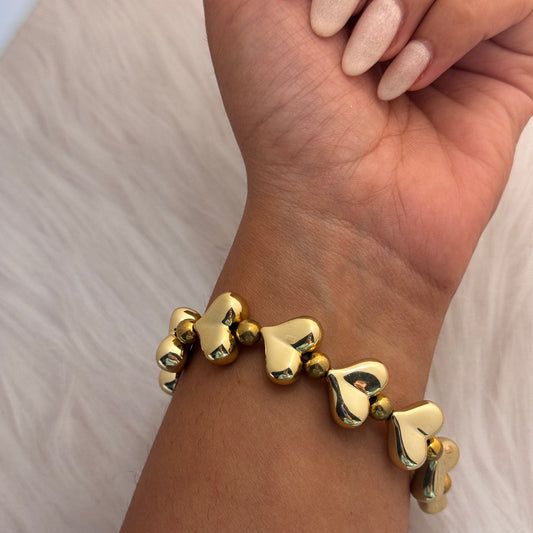 Gold heart-shaped bracelet on a wrist with a neutral background