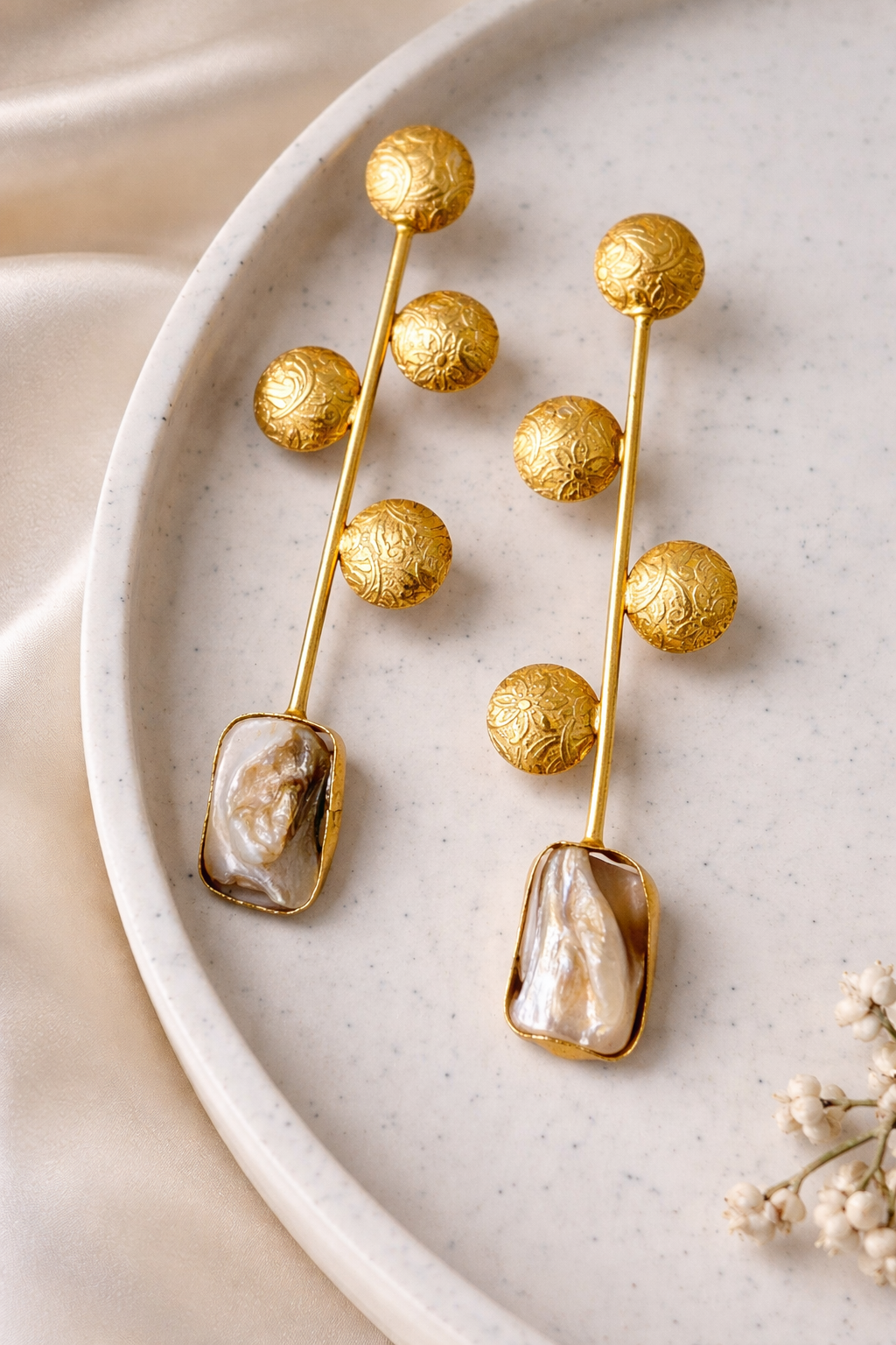 Gold earrings with pearl-like stones on a white plate