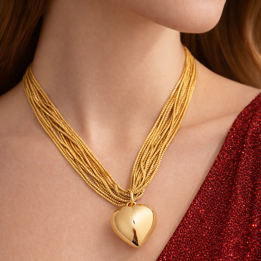 Gold necklace with a heart pendant worn by a person in a red outfit