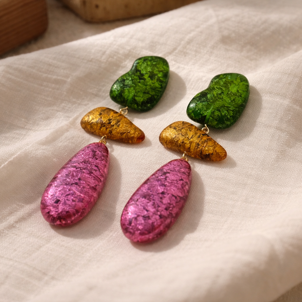 Pair of earrings with pink and gold teardrop shapes on a beige fabric background