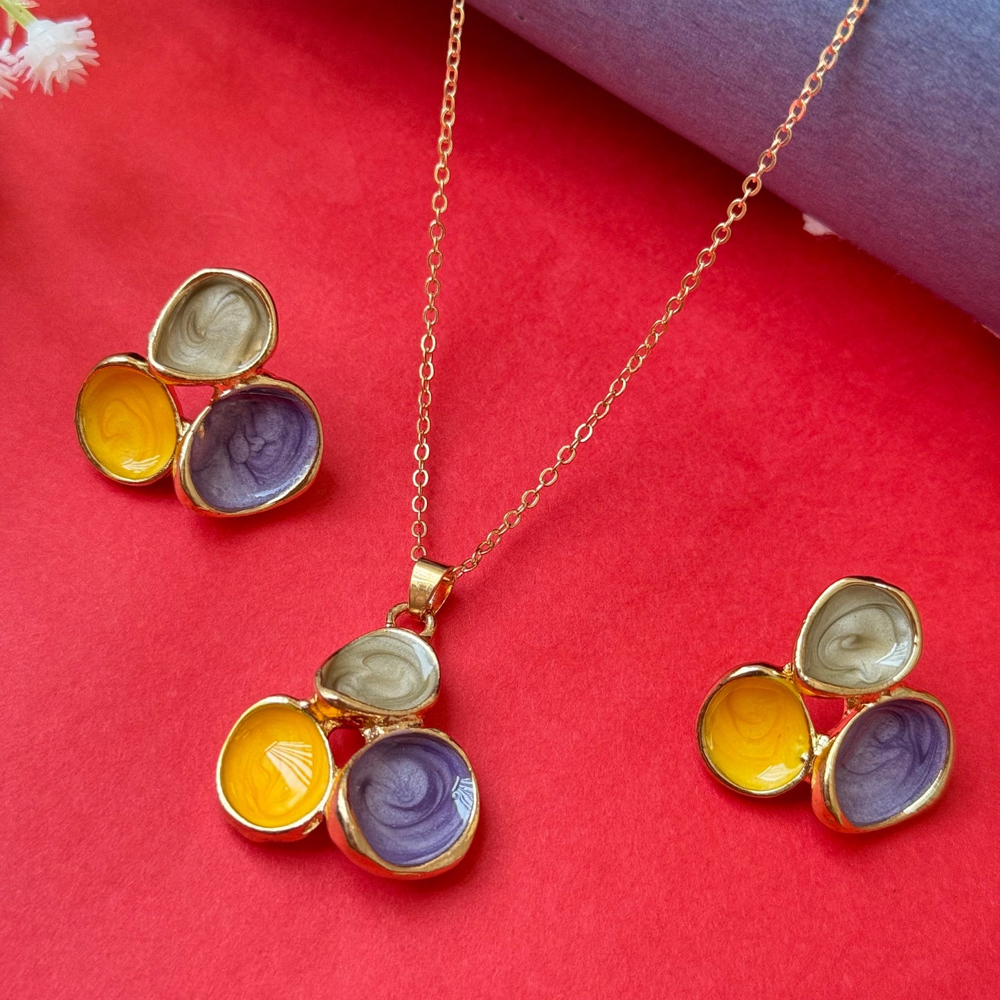 A multicolored chain and pendant set with gold-colored metal and multicolored stones, displayed against a red background with a floral pattern.