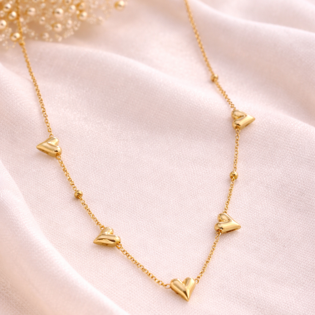 Gold necklace with heart-shaped pendants on a soft pink fabric background