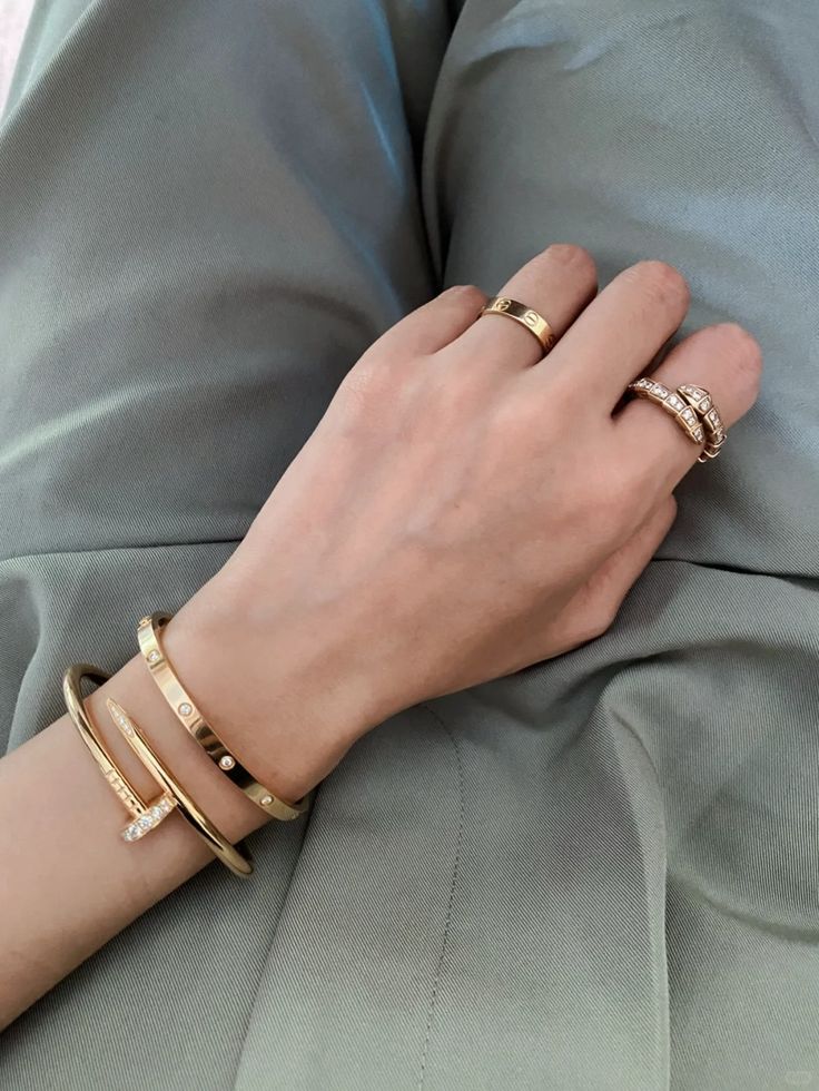 Hand wearing gold bracelets and rings on a gray fabric background