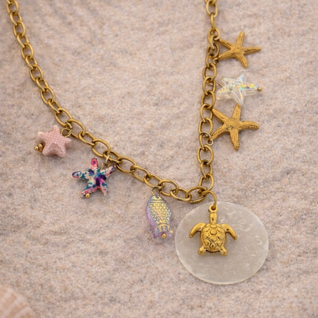 Necklace with starfish, turtle, and seashell charm on a sandy background