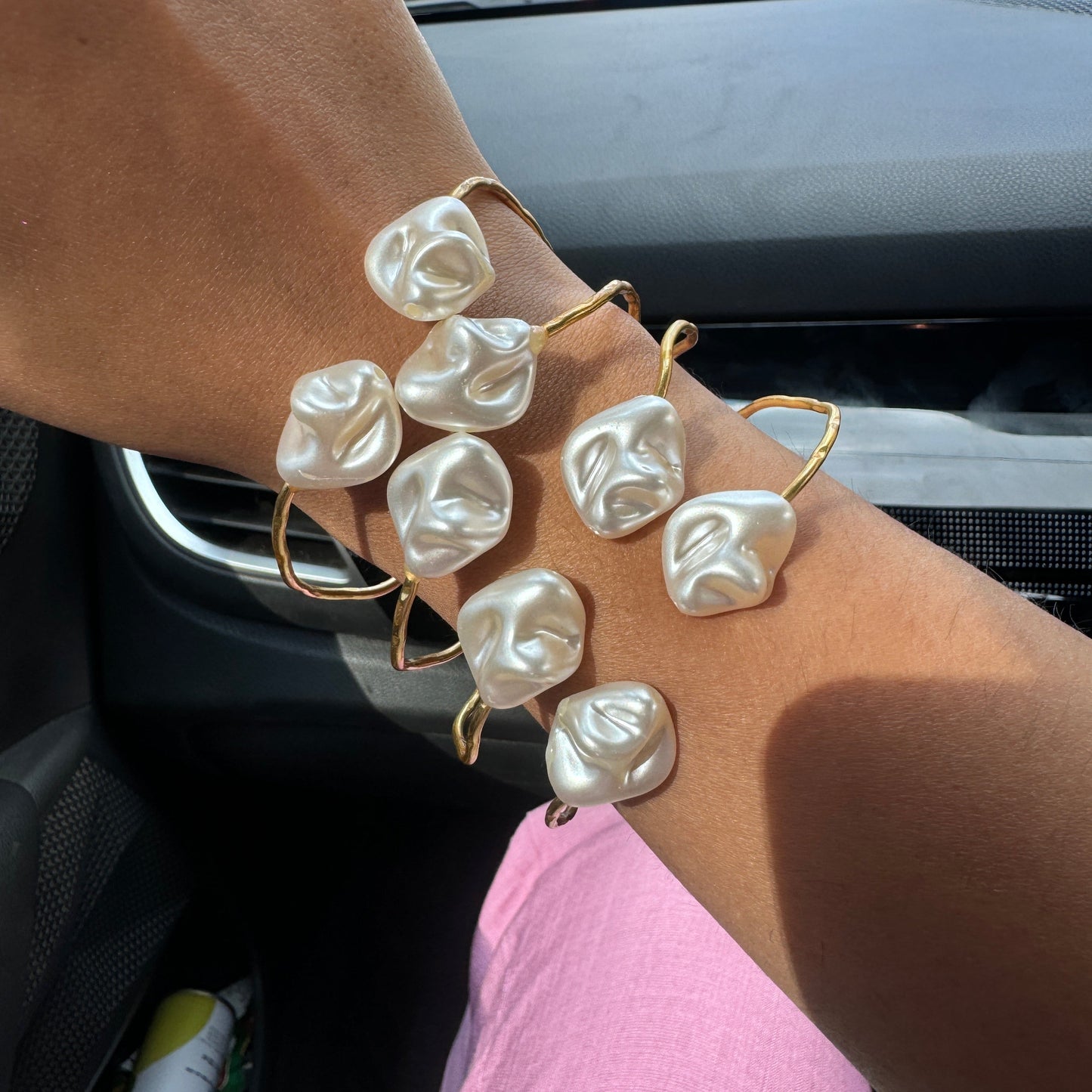Hand wearing a pearl bracelet with a blurred city street view in the background