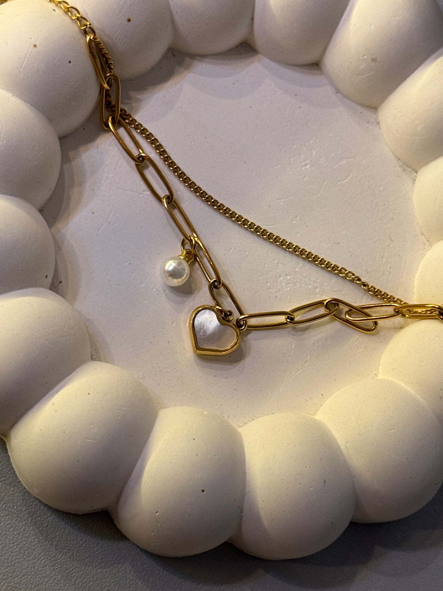Gold chain necklace with heart and pearl charm on a white textured surface