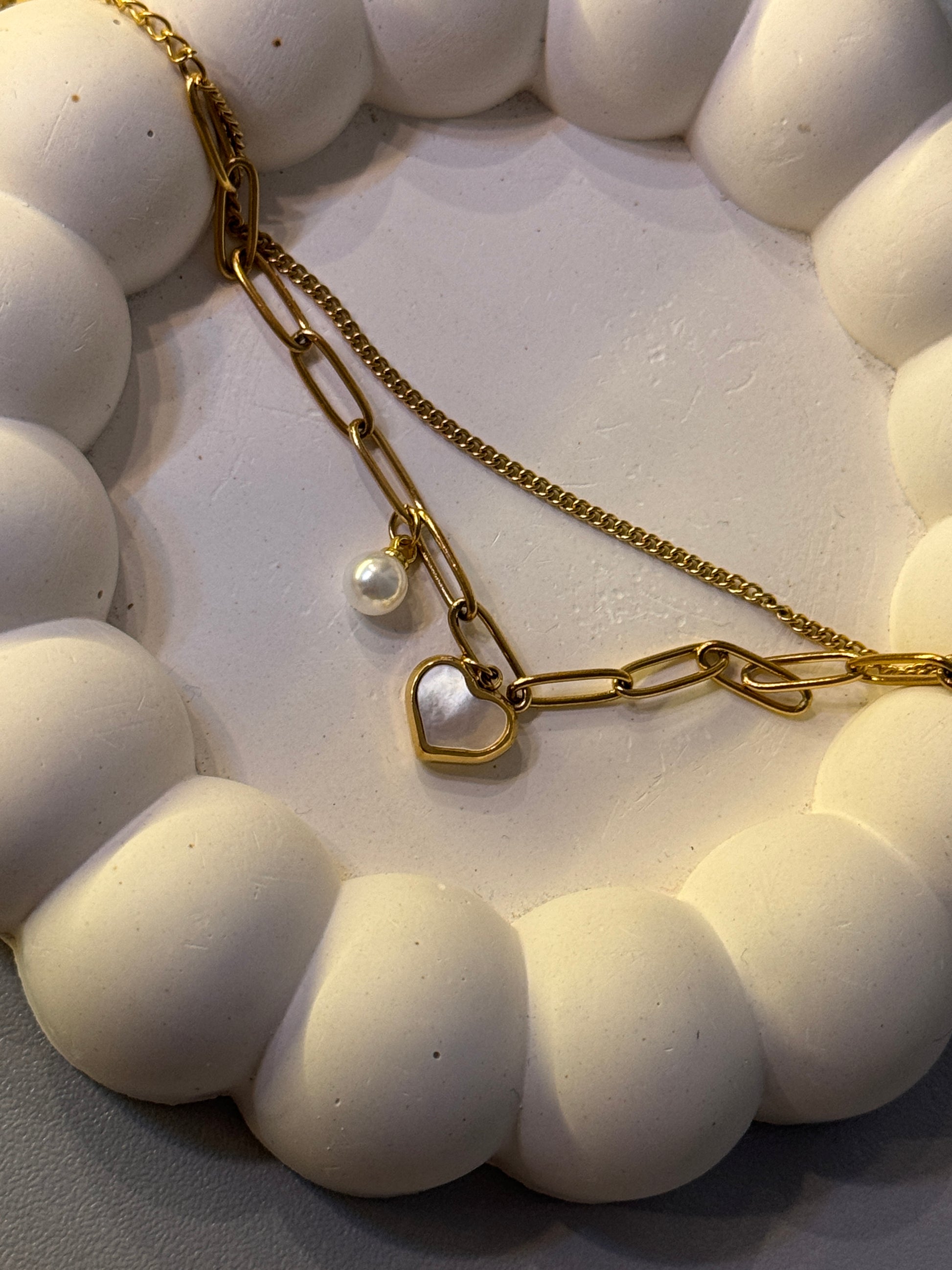 Gold chain necklace with heart and pearl charm on a white textured surface