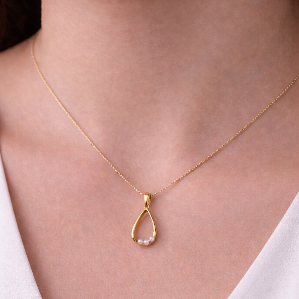 Gold necklace with a pendant on a person wearing a white top