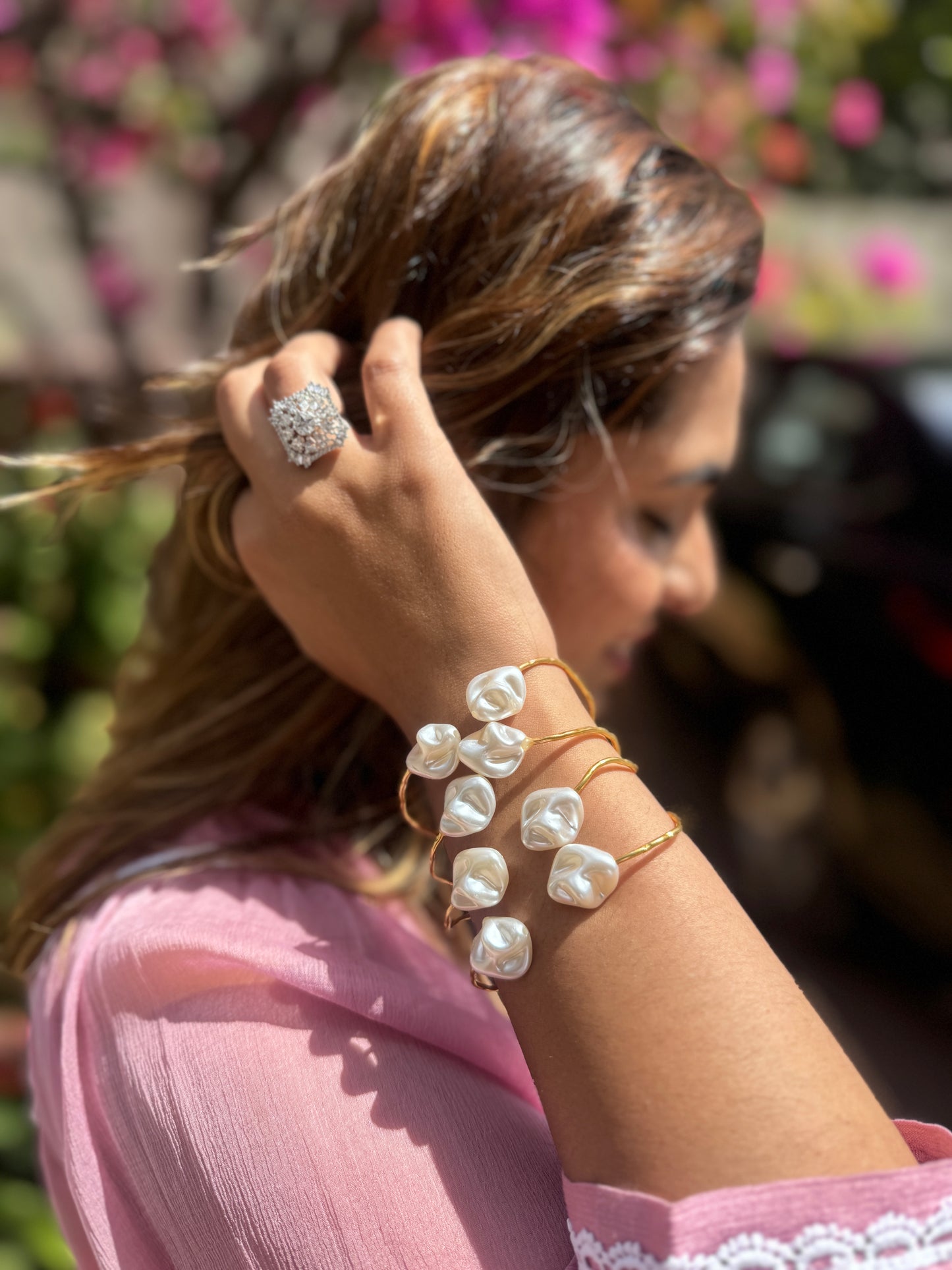 Woman with pearl bracelet and ring adjusting hair against a blurred floral background