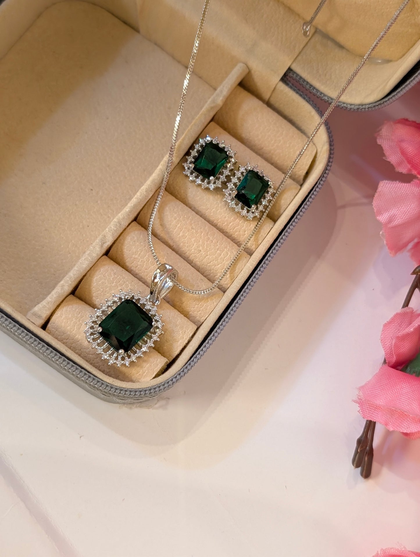 Jewelry set with green gemstones in a beige jewelry box on a pink floral background