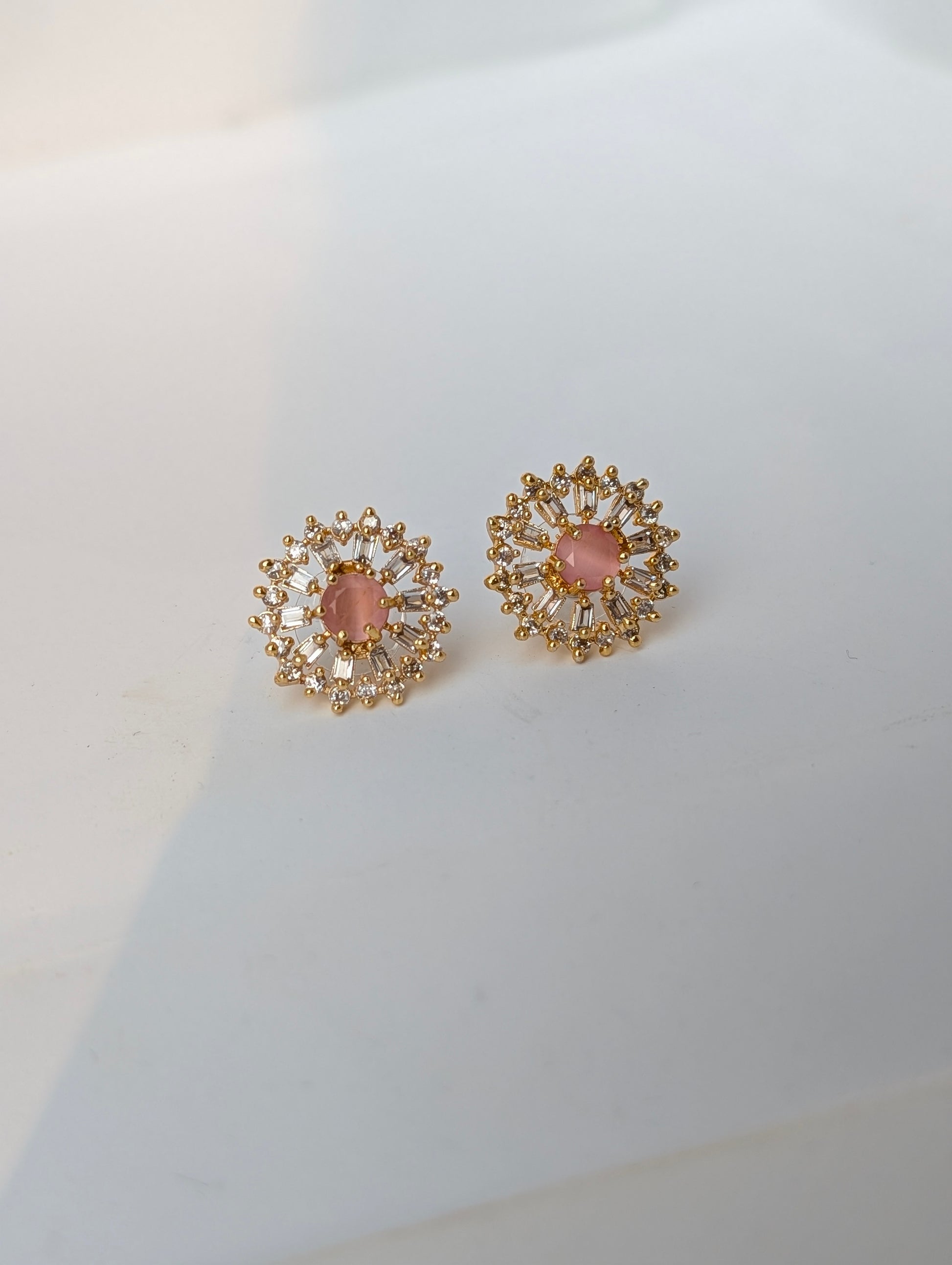 Pair of gold earrings with pink gemstones on a white background