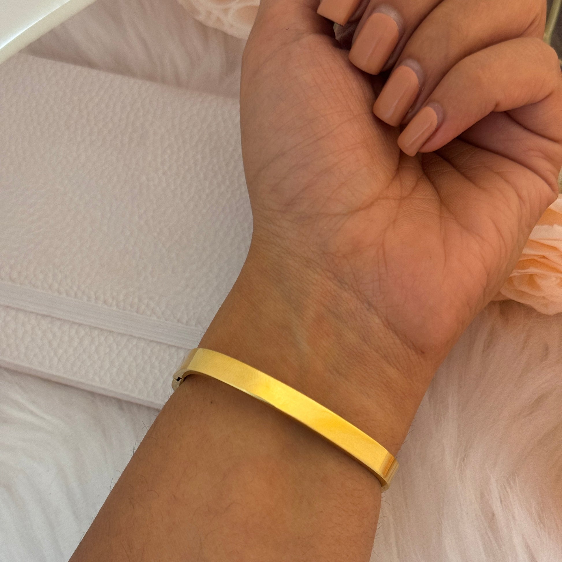 Gold bracelet on a wrist with a neutral background