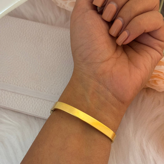 Gold bracelet on a wrist with a neutral background