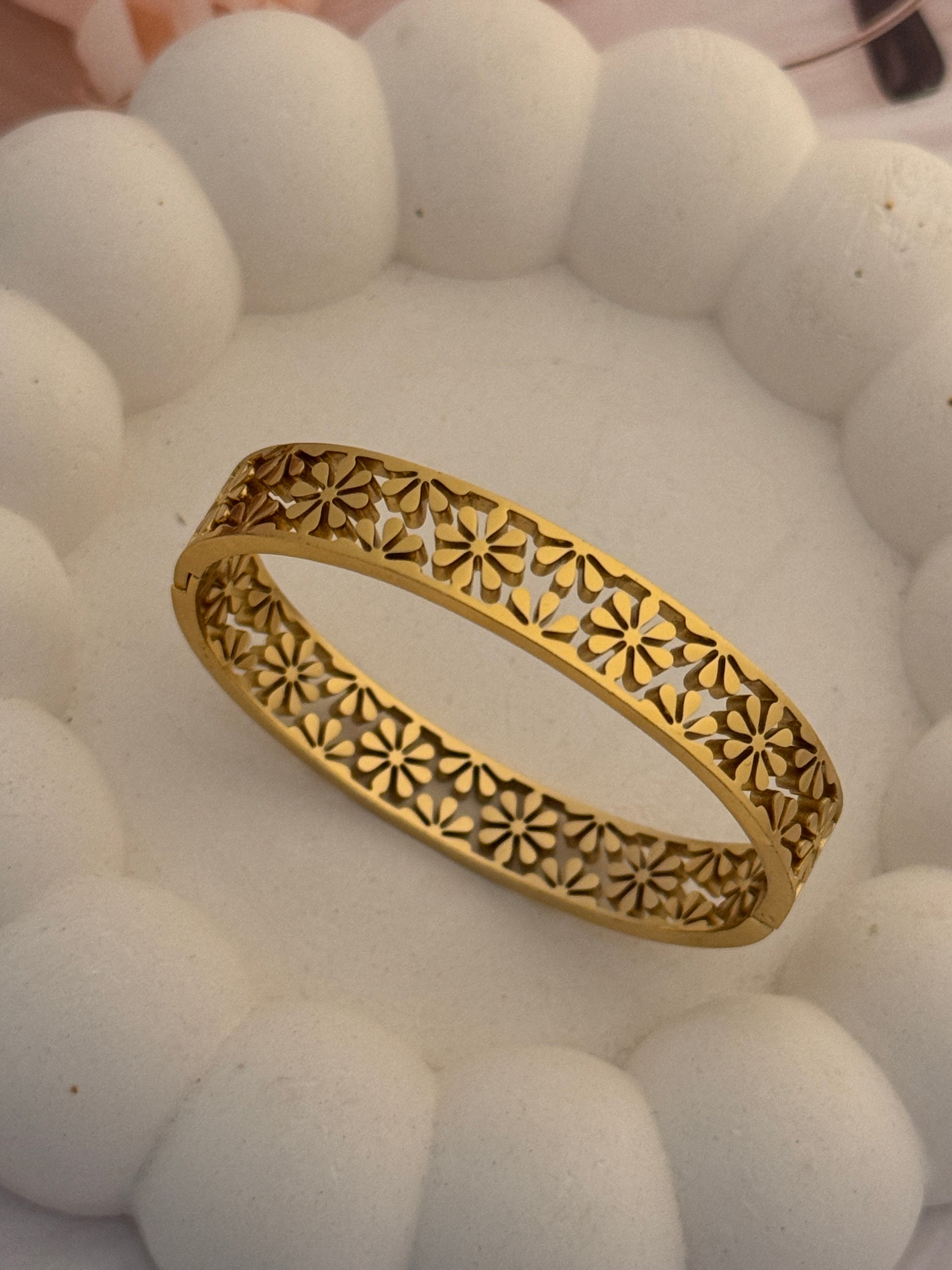 Gold bracelet with intricate design on a textured white background