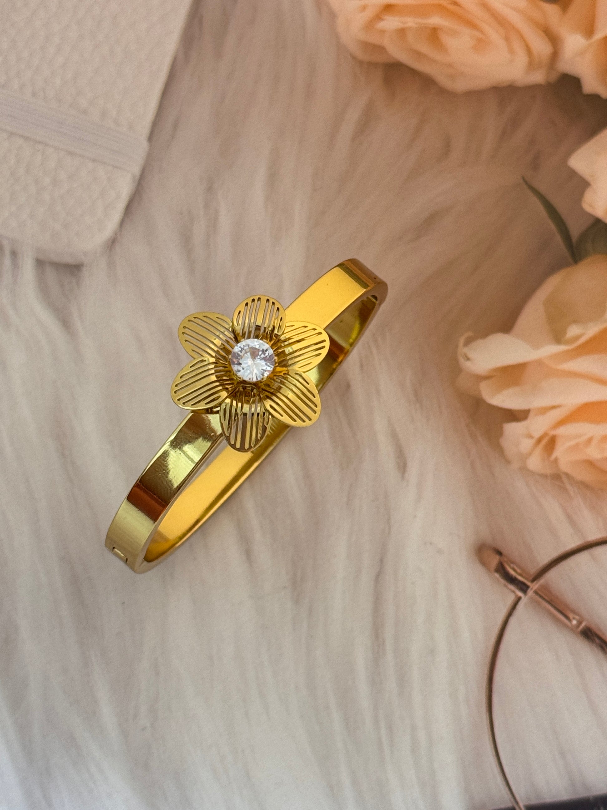 Gold bracelet with a floral design and diamond on a light wooden surface with flowers.