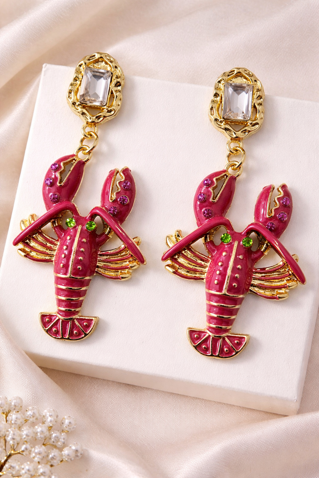 Lobster-shaped earrings on a white box with a soft pink background