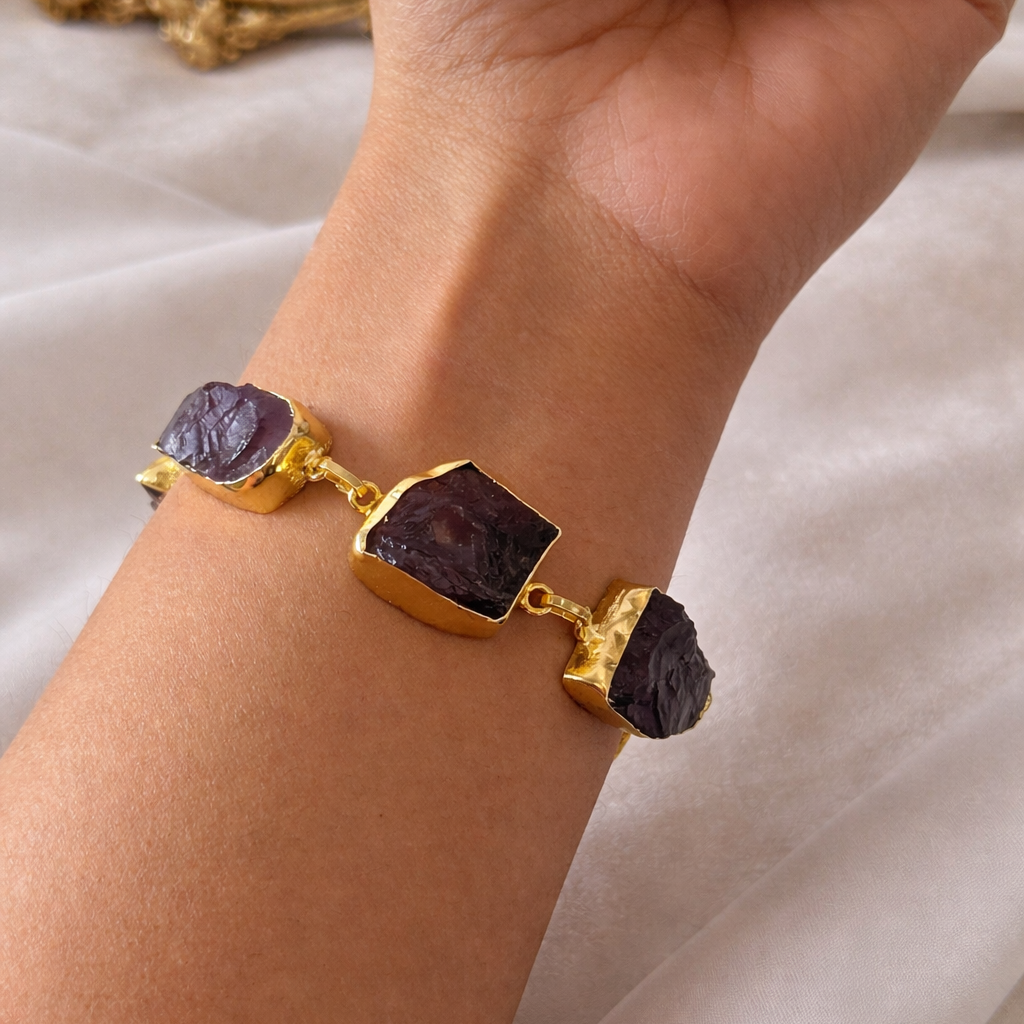 Gold bracelet with dark stones on a wrist against a soft background
