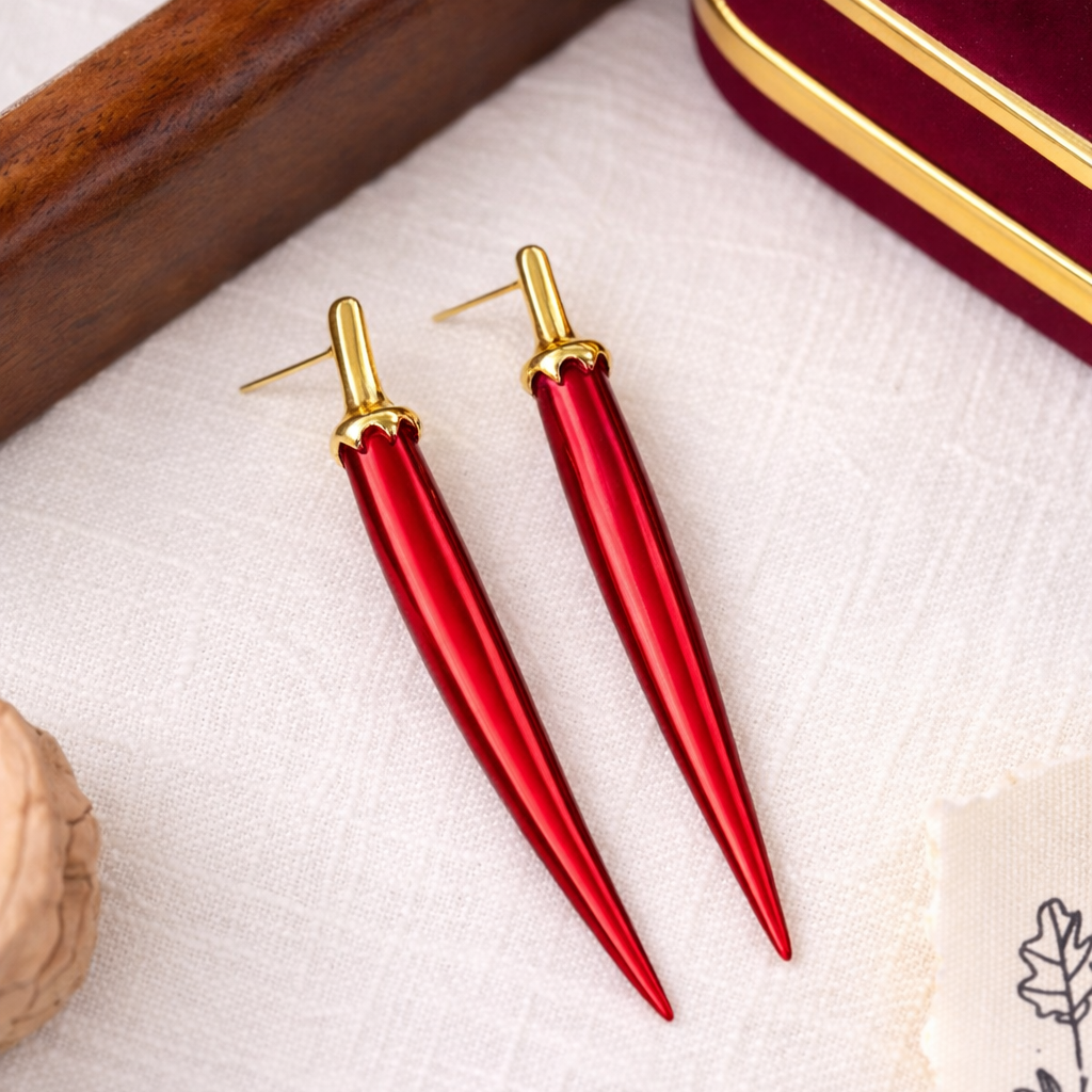 Red earrings with gold accents on a textured surface with a jewelry box in the background.