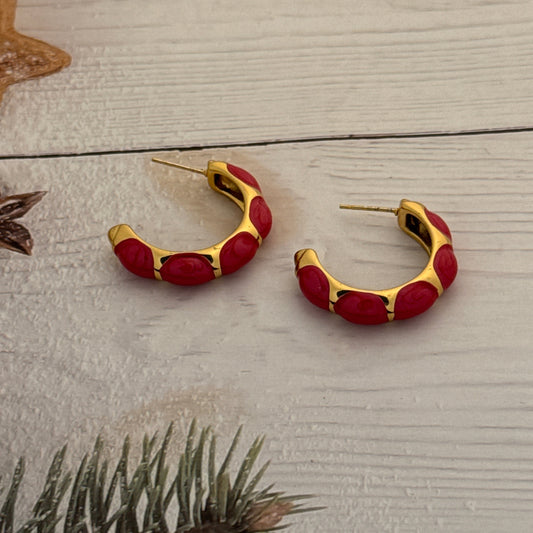 Red and gold earrings on a wooden surface with a plant in the corner