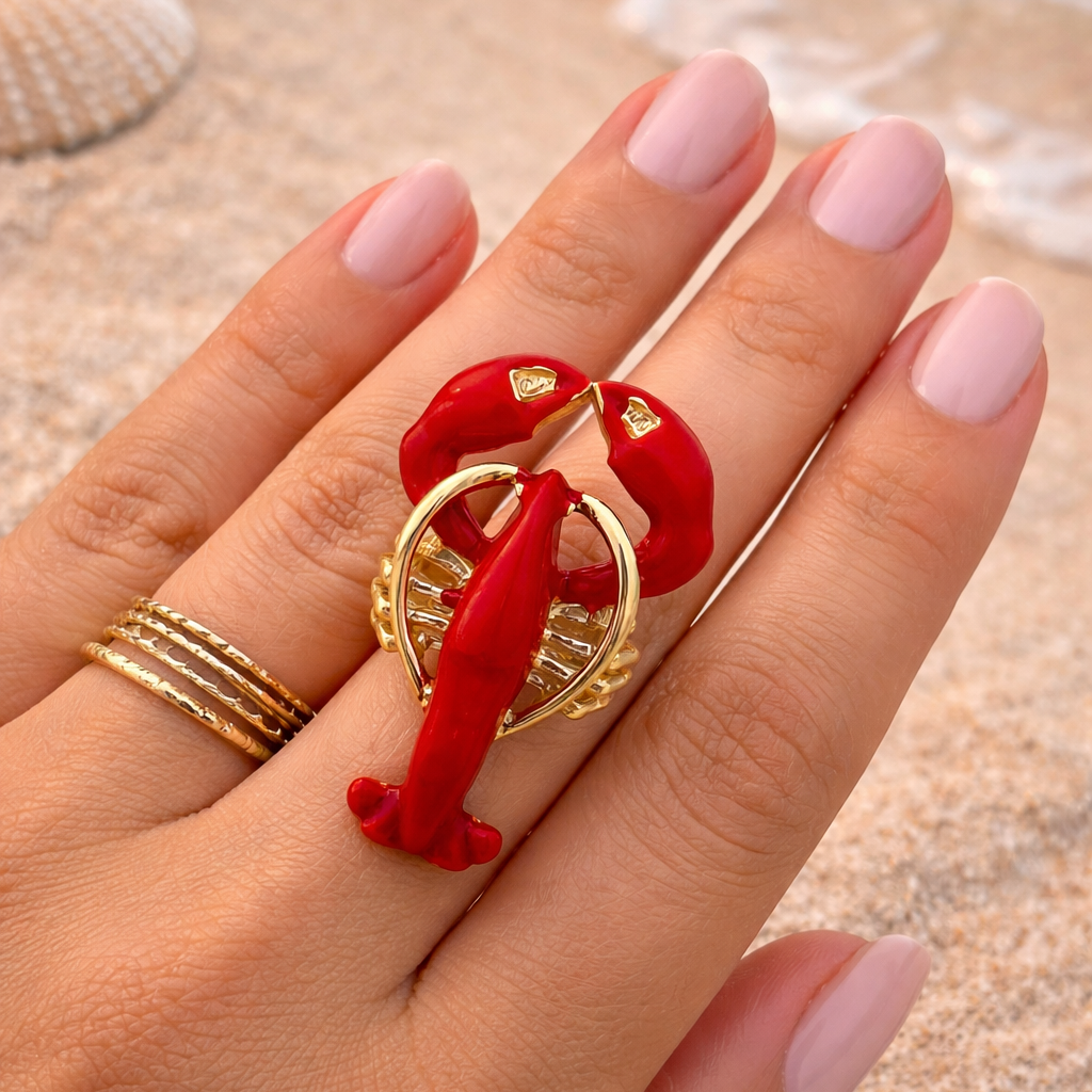 Hand wearing a red lobster-shaped ring on a beach background