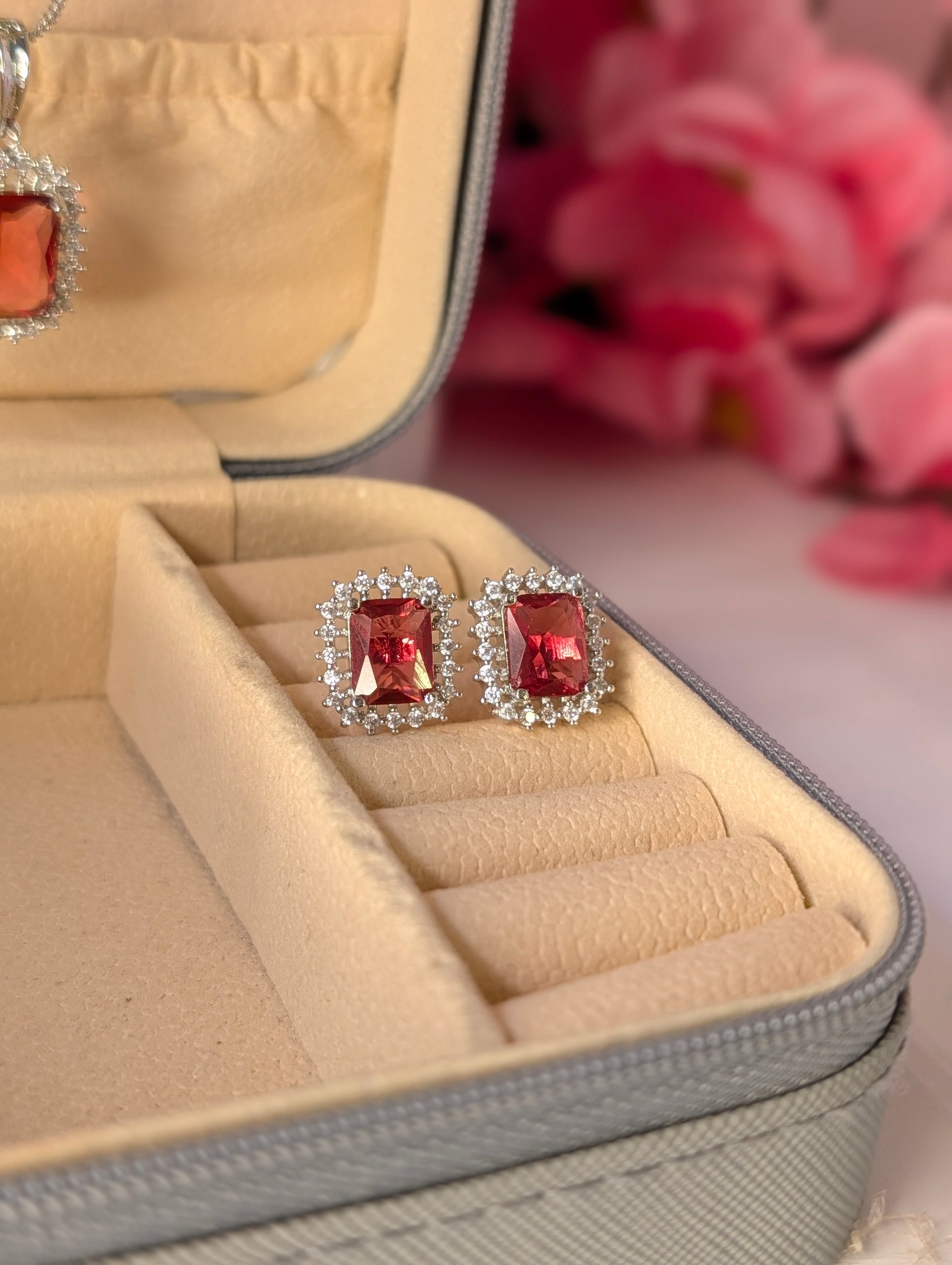 Red gemstone earrings in a jewelry box with pink flowers in the background