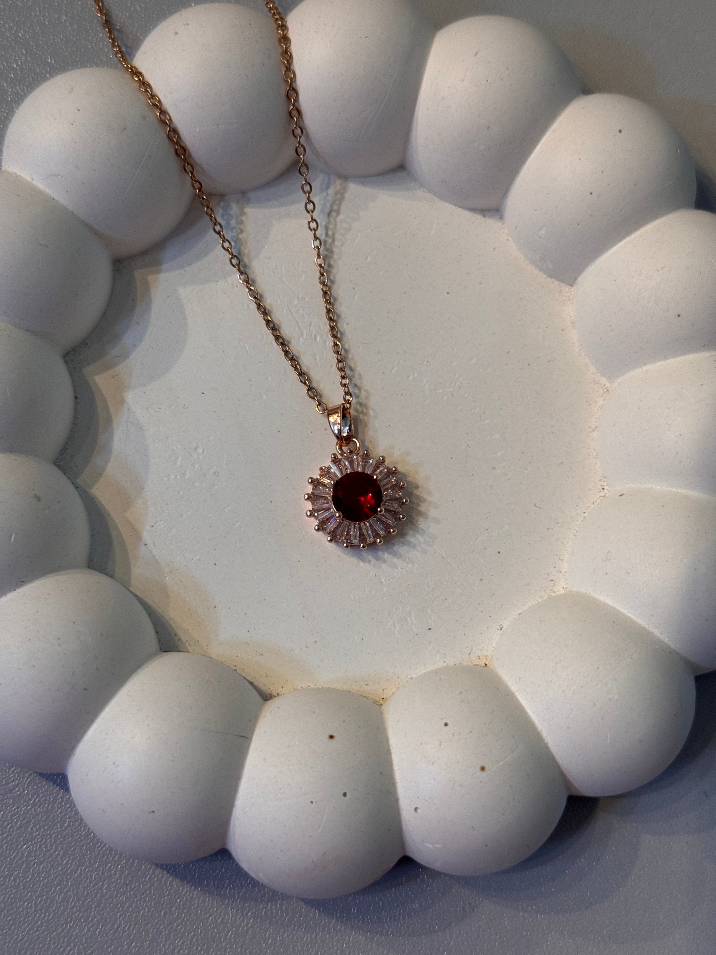 Close-up of a necklace with a red gemstone on a textured white surface