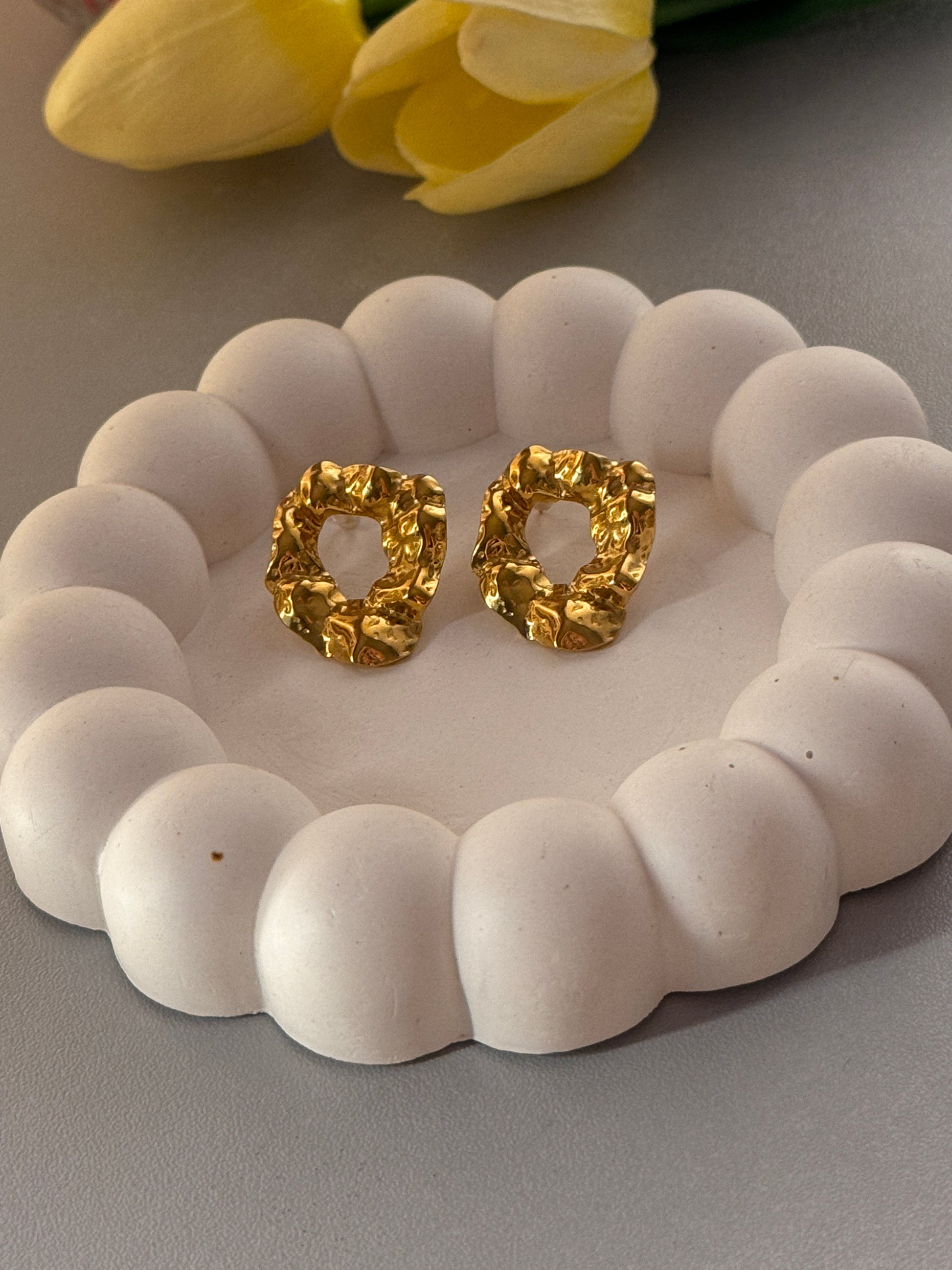 Gold earrings on a white stone surface with a yellow flower in the background