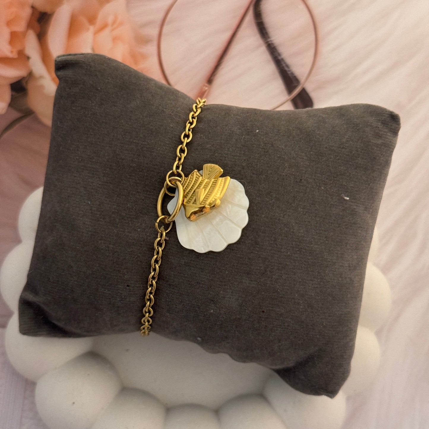 Gold bracelet with a white shell charm on a gray pillow