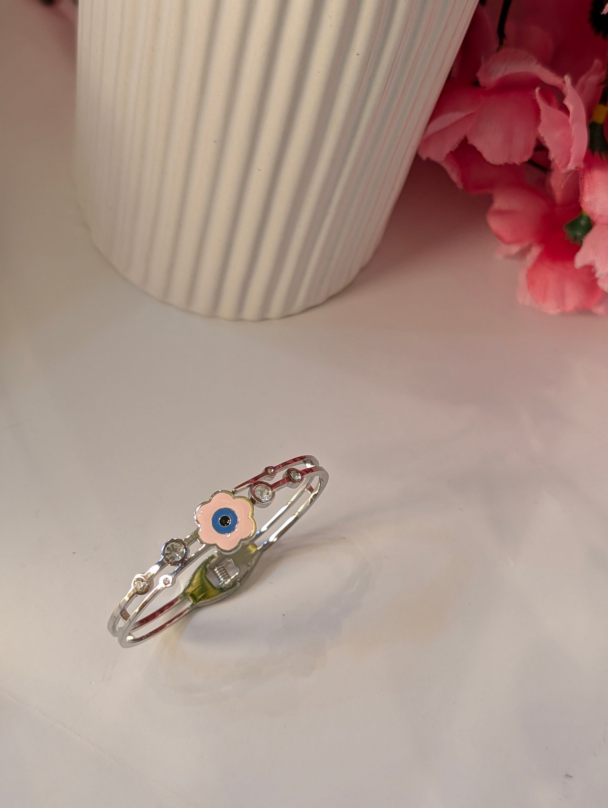 Silver ring with a floral design on a light surface with pink flowers and a white vase in the background.