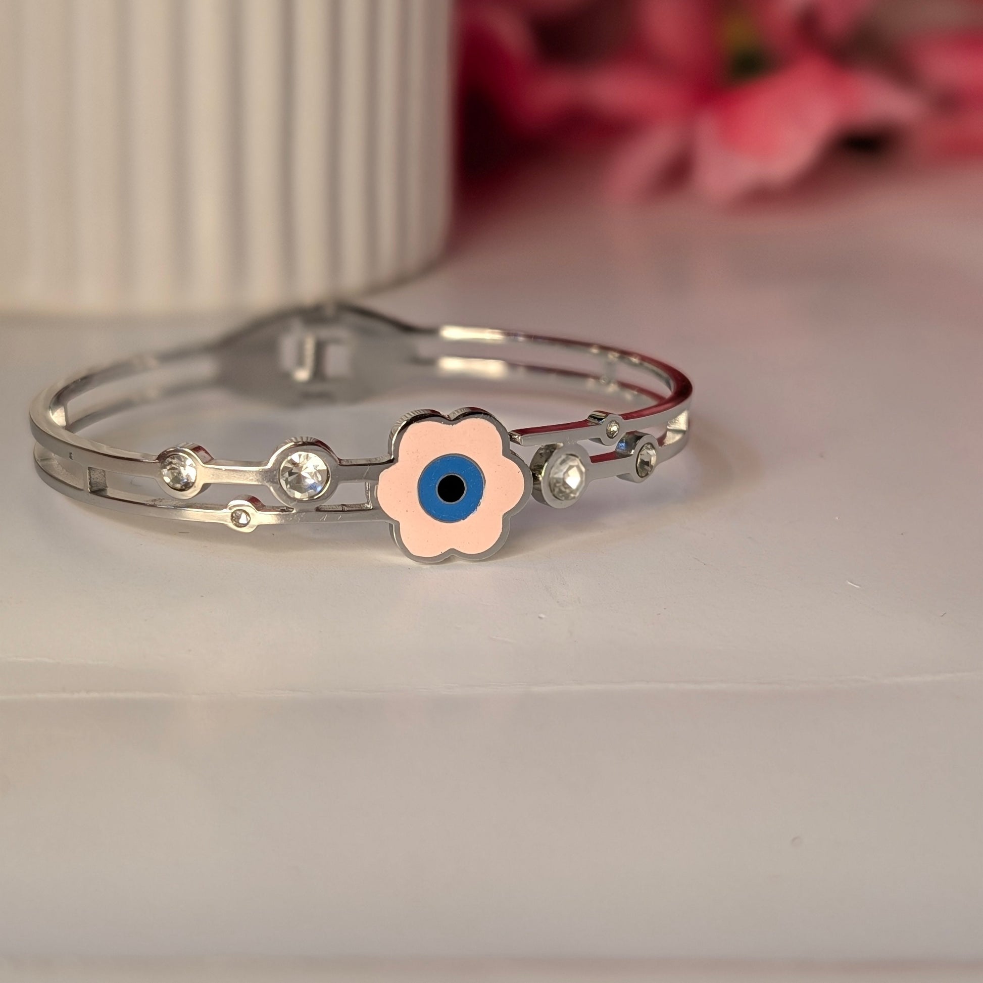 Silver bracelet with a pink flower charm featuring a blue eye on a light surface.