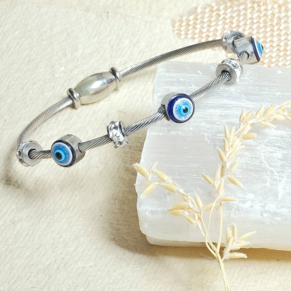 Silver bracelet with blue evil eye charms on a white stone with natural elements