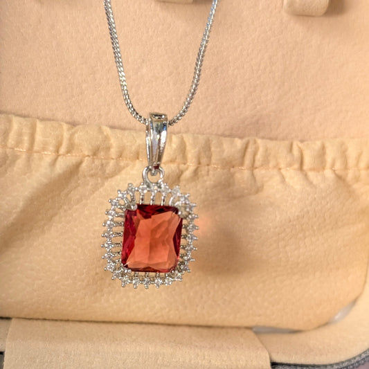 Silver pendant with a red gemstone on a beige background